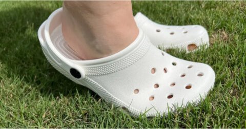 Pie con Crocs sobre césped, comparación de calzado tradicional versus barefoot para BareMotion, destacando cómo los zapatos barefoot promueven una alineación natural del pie frente a alternativas convencionales