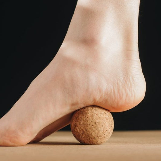 Pie utilizando una pelota de corcho para masaje y relajación, promoviendo la salud del pie en combinación con el uso de calzado barefoot de BareMotion