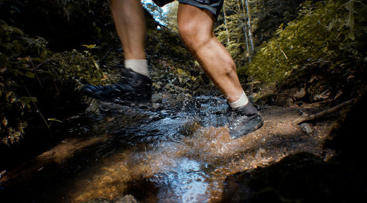 Persona cruzando un arroyo usando zapatos barefoot de BareMotion, demostrando la durabilidad y adaptabilidad del calzado en condiciones naturales